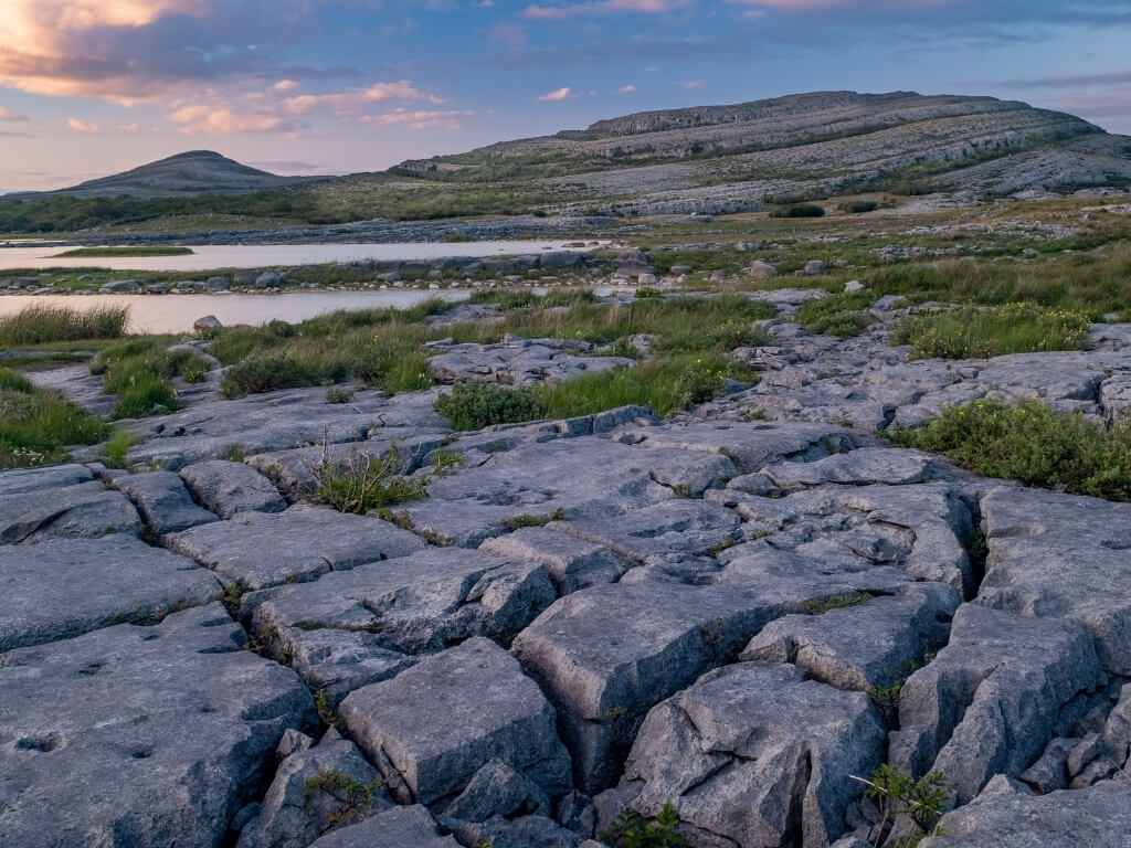 A picture of the unique grey limestone landscape of the Burren National Park with patches of green grasses and hills in the background