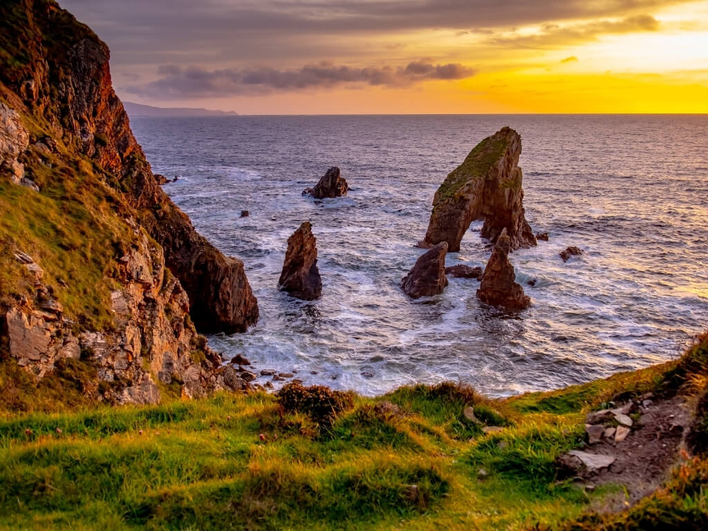 A picture of the sun setting over the Donegal coast of Ireland with the Crohy sea arch in the foreground and craggy rocks to the side