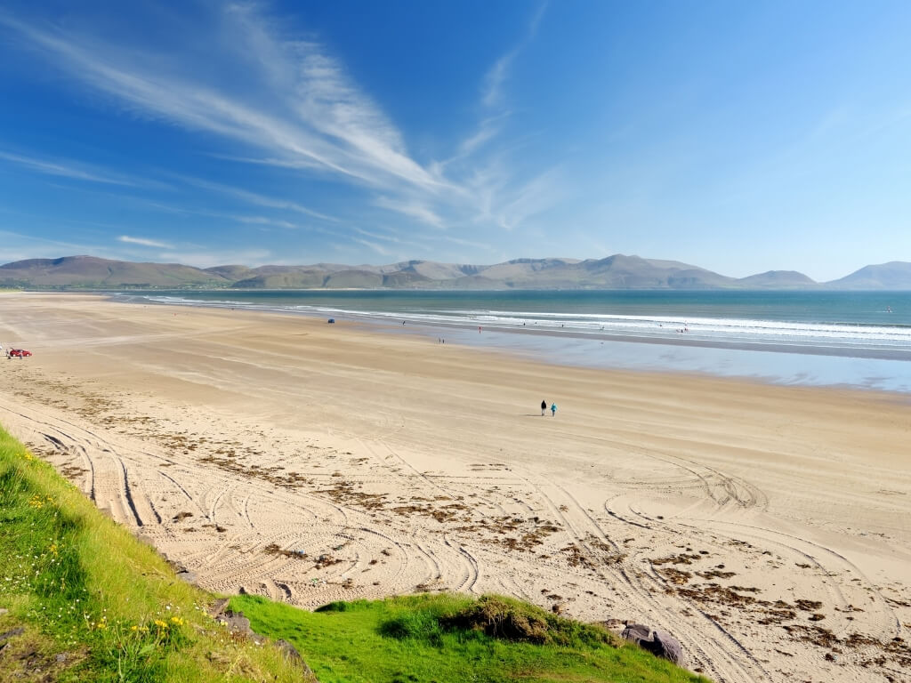 A picture of th elong sandy beach at Inch on the Dingle Peninsula in Ireland with two people walking along it and blue skies overhead