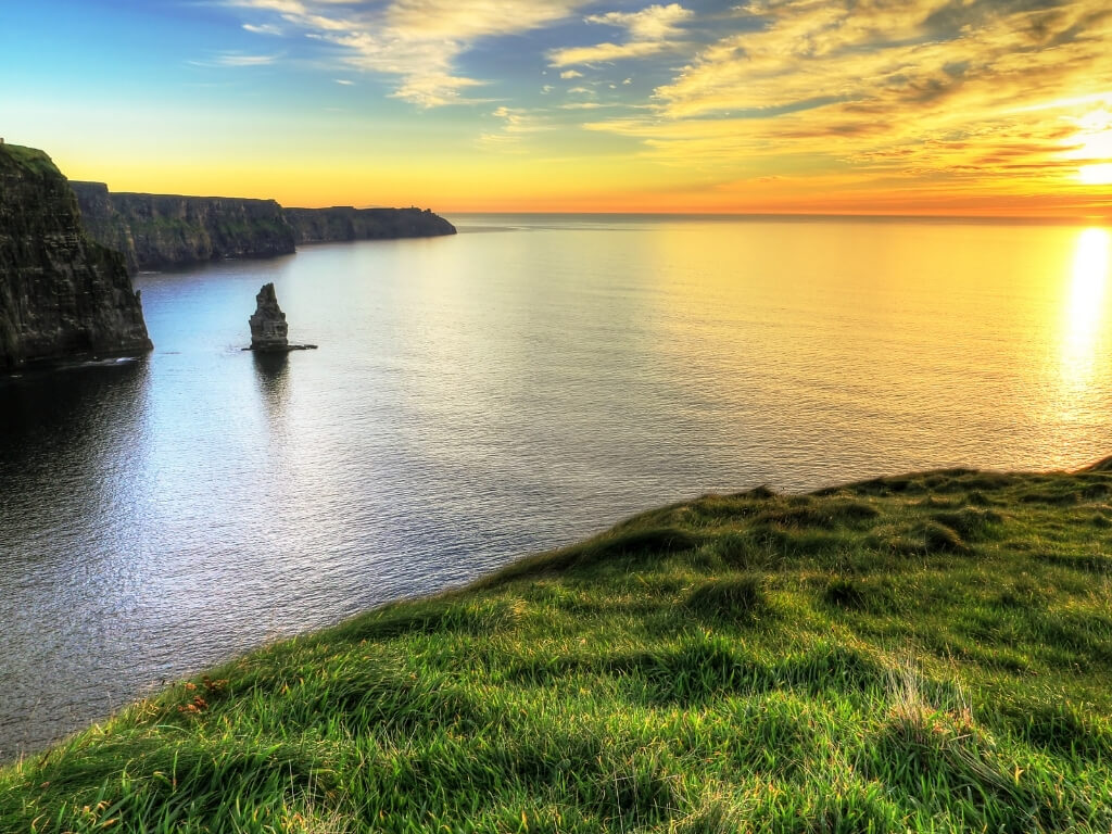 A picture of the sun setting in the distance, lighting up the Cliffs of Moher along Ireland's Wild Atlantic Way.