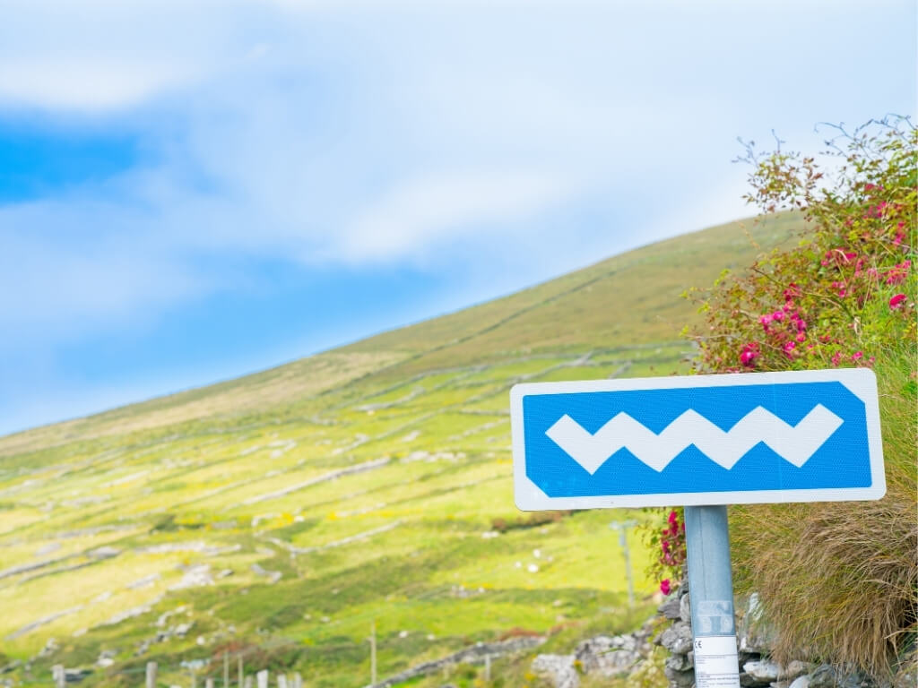 A blue Wild Atlantic Way road sign in Ireland with grassy hills behind it