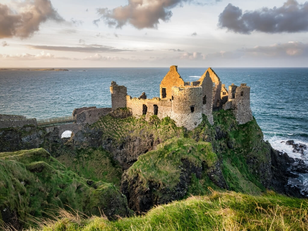 A picture of the ruins of Dunluce Castle on the Causeway Coast in Antrim with sunlight bathing it and the sea in the background