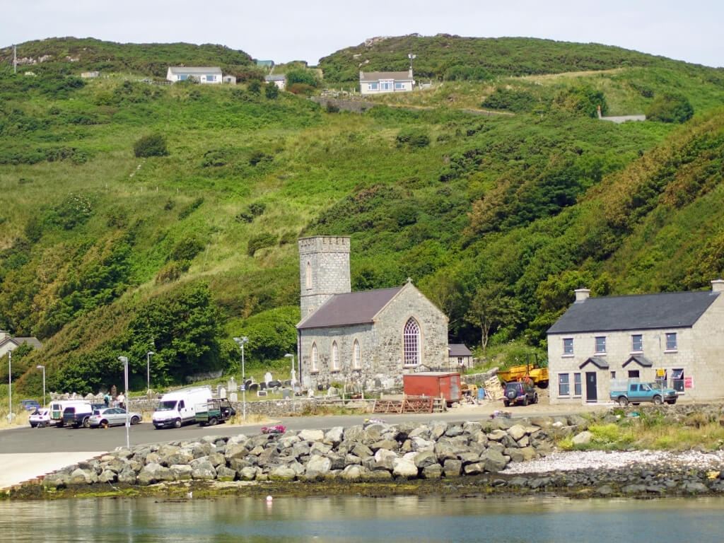 A picture of buildings at the harbour side on Rathlin Island, Antrim with a green grassy hill in the background