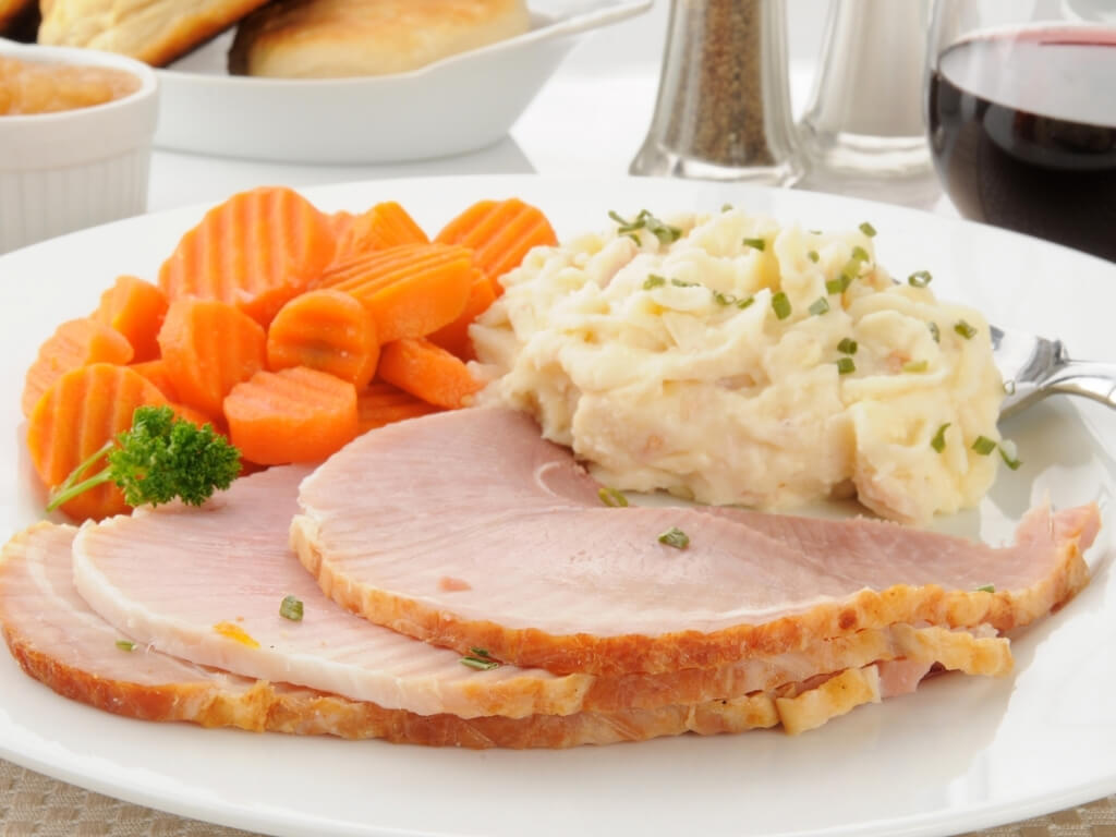 A picture of a plate containing slices of boiled ham, mashed potato, carrots and broccoli