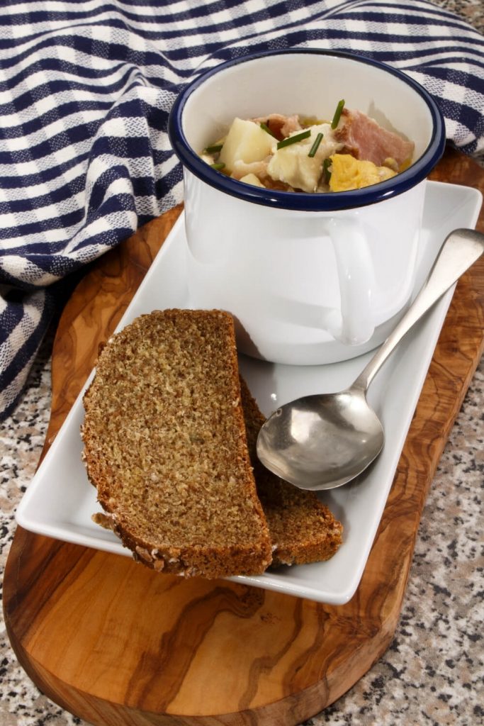 A picture of seafood chowder served in a cup with two slices of Irish soda bread presented on a wooden tray