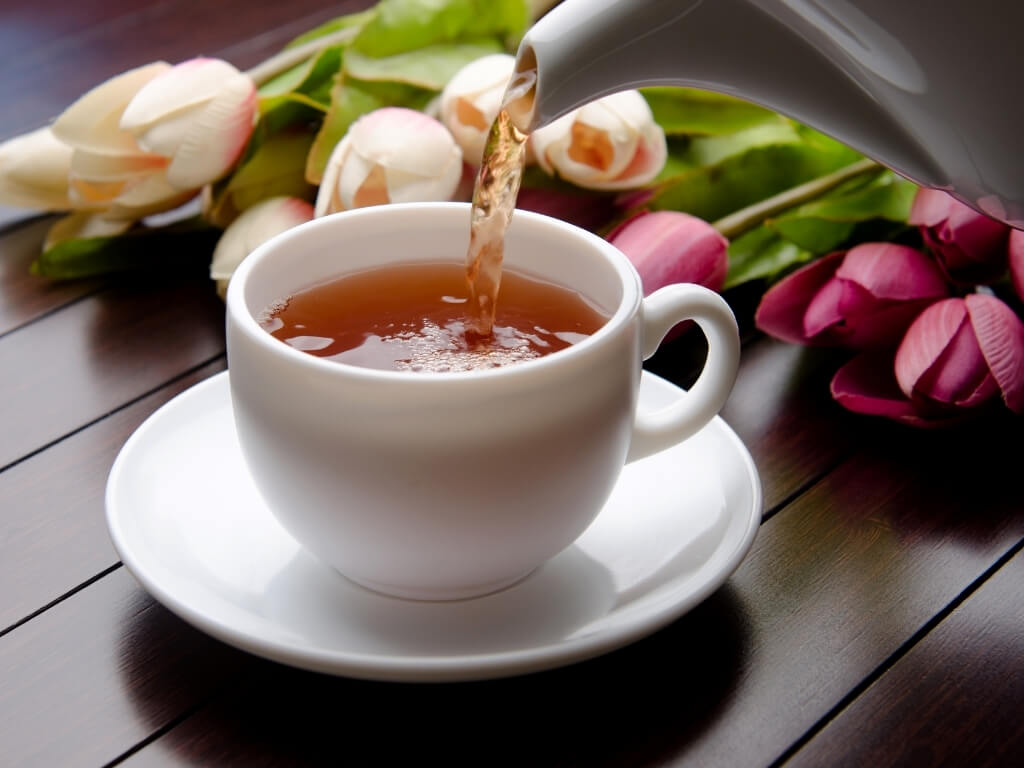 A picture of a cup of tea being poured into a teacup on a saucer