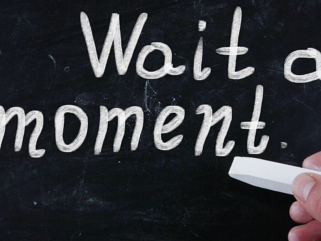 A picture of a chalk board with the words "wait a moment" written on it in chalk