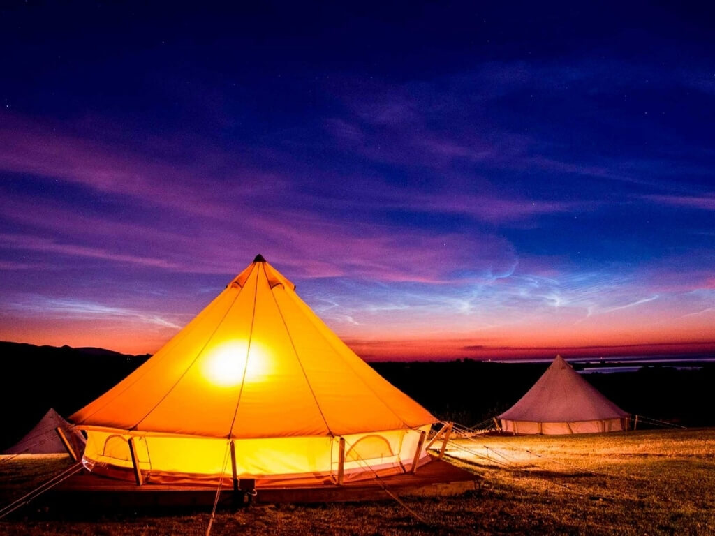 A picture of some of the bell tents at Knockrobin Glamping lit from within at night