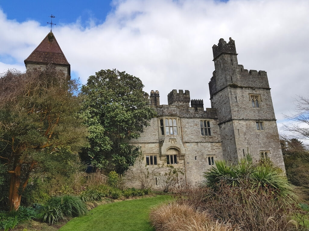 A picture of Lismore Castle in Waterford with green grass and plants leading to the castle building