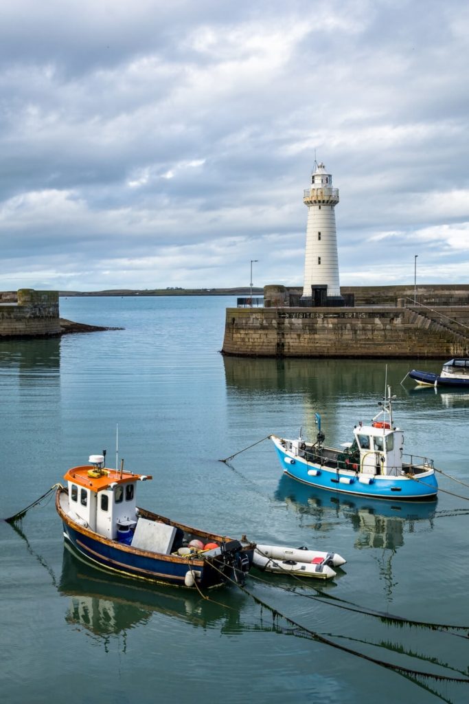 A picture of the Donaghadee Lighthouse at the end of the harbour wall with boats on the water in the foreground