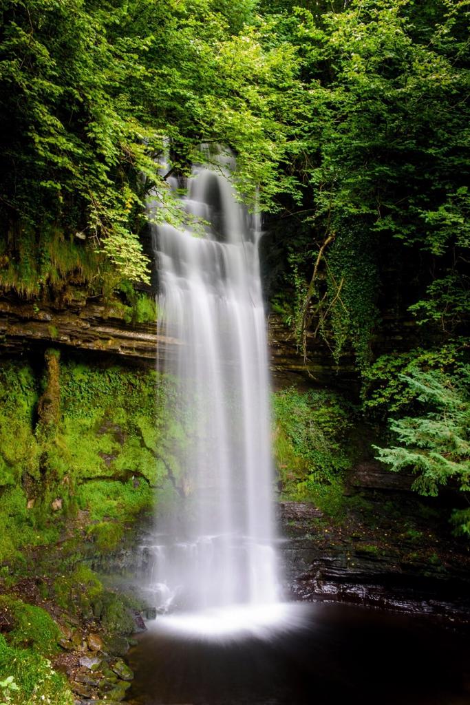 A picture of the beautiful Glencar Waterfall surrounded by lush green trees and shrubs