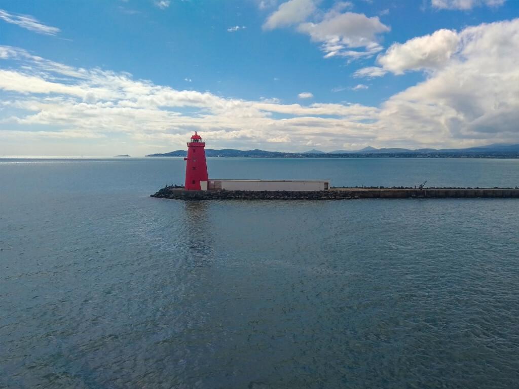 A picture of the distinctive red Poolbeg Lighthouse in Dublin bay with view across to Sugar loaf Mountain in Wicklow in the background