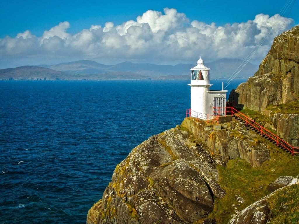 A picture of the white tower of Sheep's Head Lighthouse looking out across the sea with mountains in the far distant background