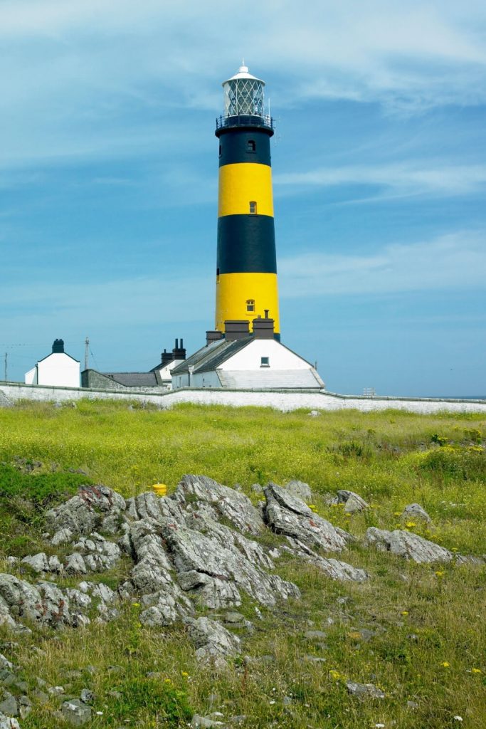 A picture of the striking black and yellow The St John's Point Lighthouse in County Down with blue skies overhead with whispy clouds