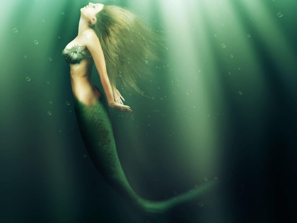 A picture of a mermaid in the water with blonde hair and a green tail