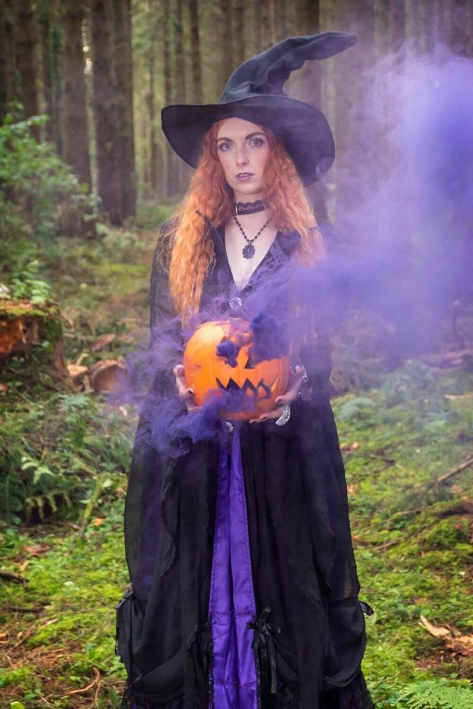 Halloween witch in a forest holding a smoking pumpkin