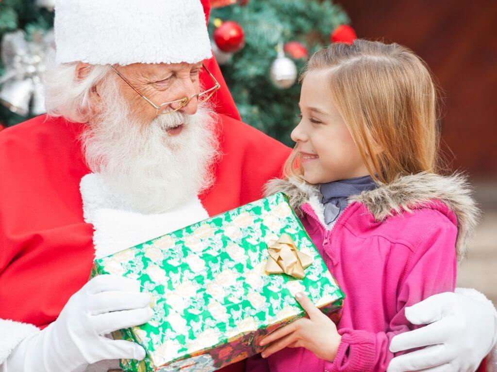 A picture of a girl in a pink coat meeting Santa Claus and receiving a present from him