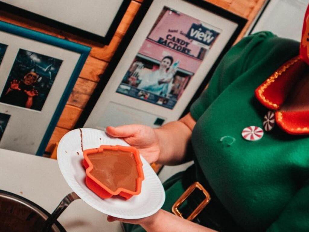 A picture of a Christmas tree mould on a plate with chocolate inside being held up by a lady in an elf costume