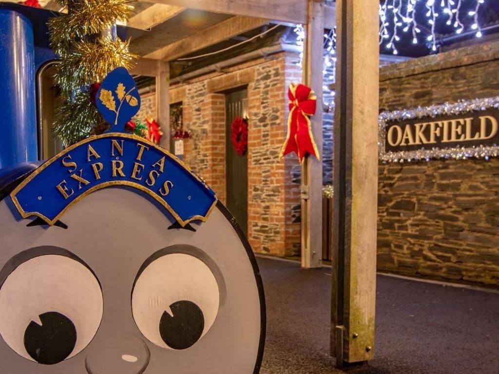 A picture of the Oakfield Park Santa Express standing in the station with a sign saying Oakfield Park with tinsel around it