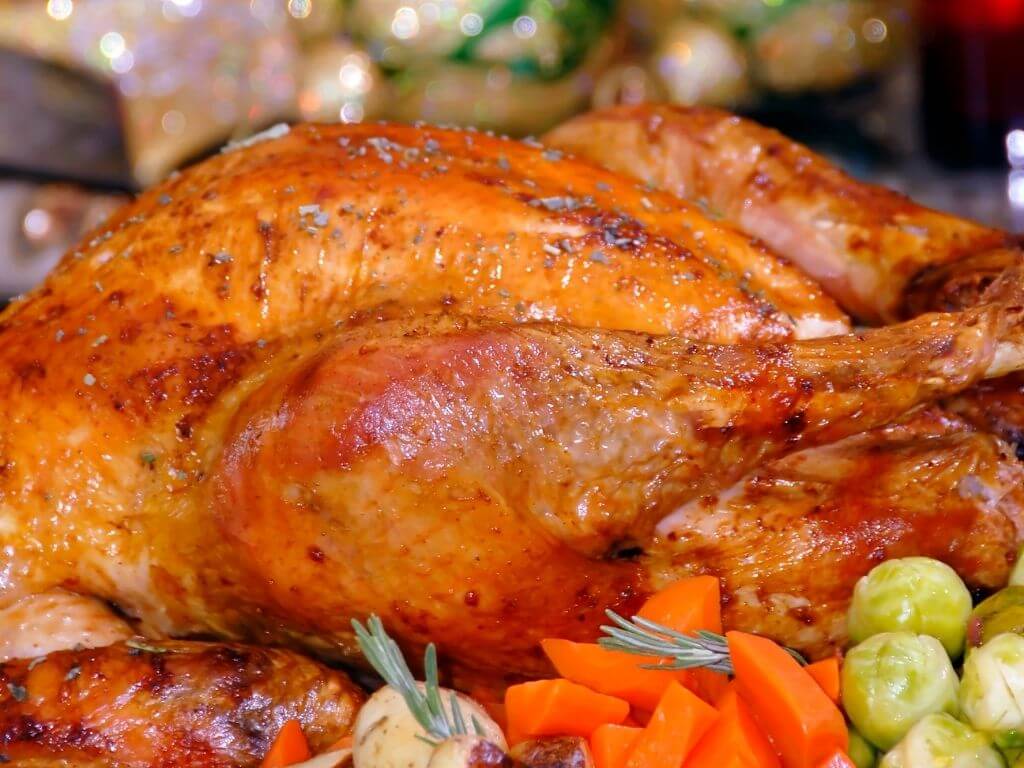 A close up picture of a roast turkey with vegetables in the foreground