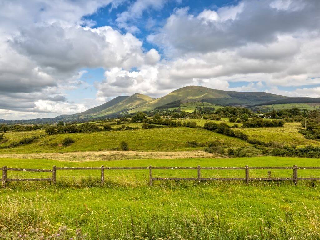 A picture of Galtymore Mountain from Tipperary with scattered blue skies overhead and rolling green fields in the foreground