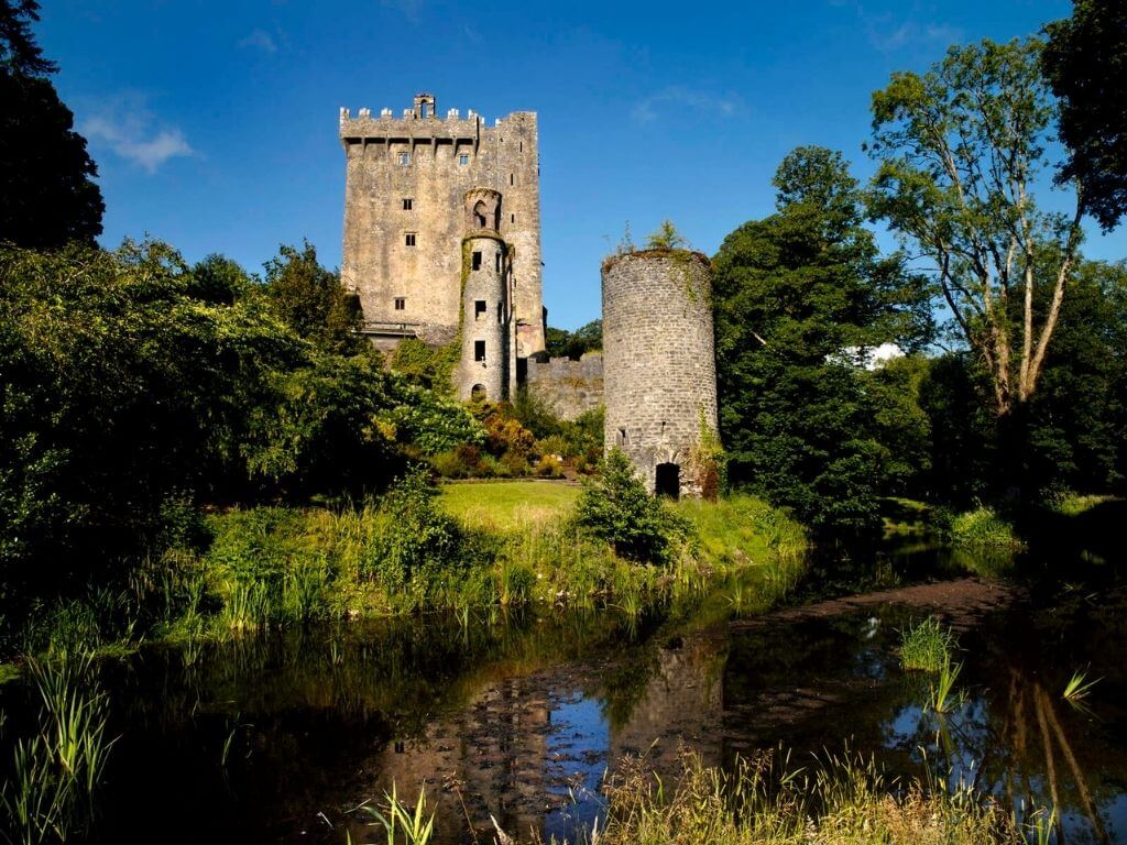 A picture of Blarney Castle from the riverside with blue skies overhead
