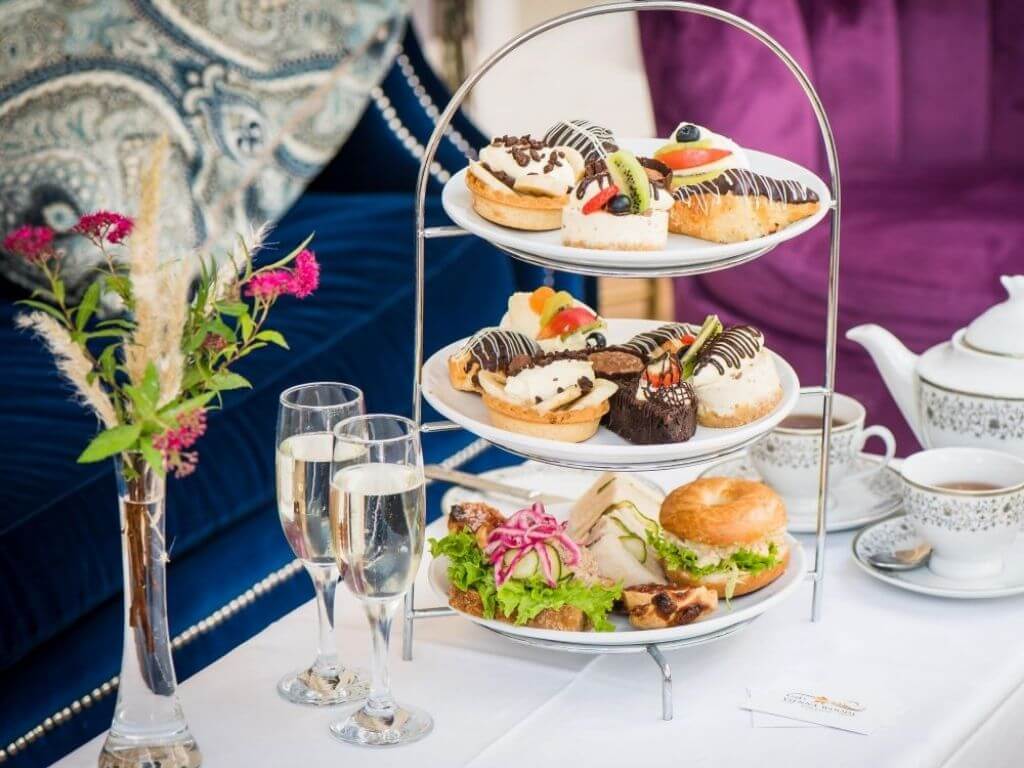A picture of three tiers of afternoon treats on a table with champagne flutes ready for the Vienna Woods Hotel Afternoon Tea