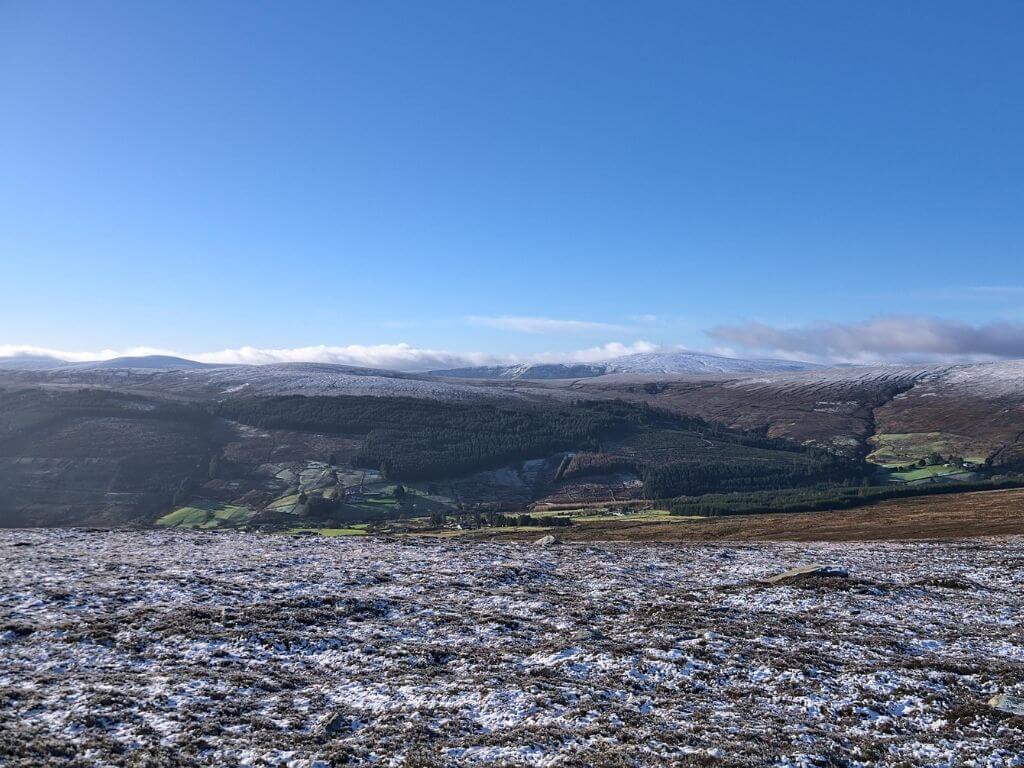 A picture of the Wicklow Mountains National Park in winter with frost on the ground in the foreground and snow on the mountains in the background