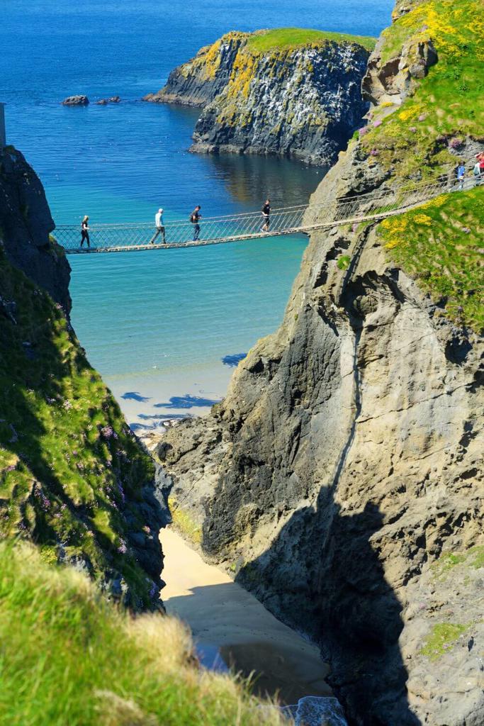 A picture of people crossing the the Carrick-a-Rede Rope Bridge in County Antrim along the Causeway Coast