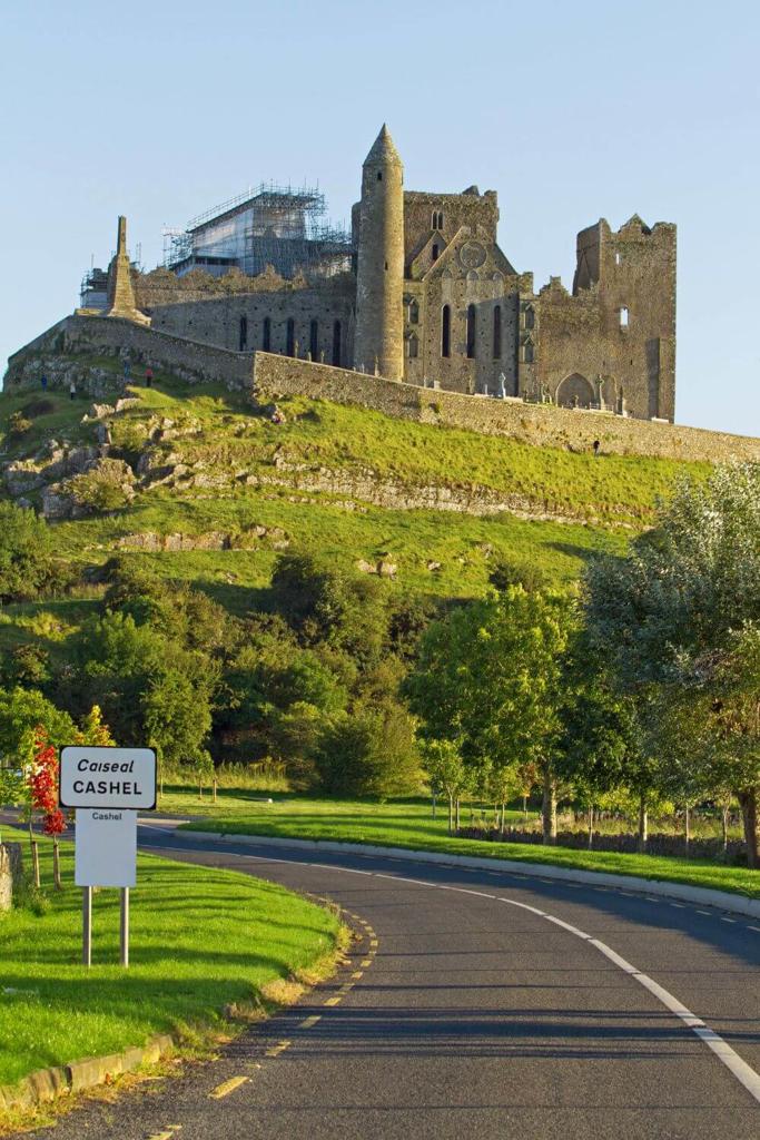 A vertical picture of the Rock of Cashel in County Tipperary, Ireland with the Rock on the hill in the background and a winding road in the foreground