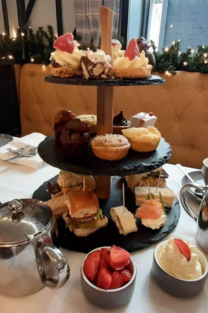 A table laid for afternoon tea with a three-tiered cake stand, teapot and other assortments