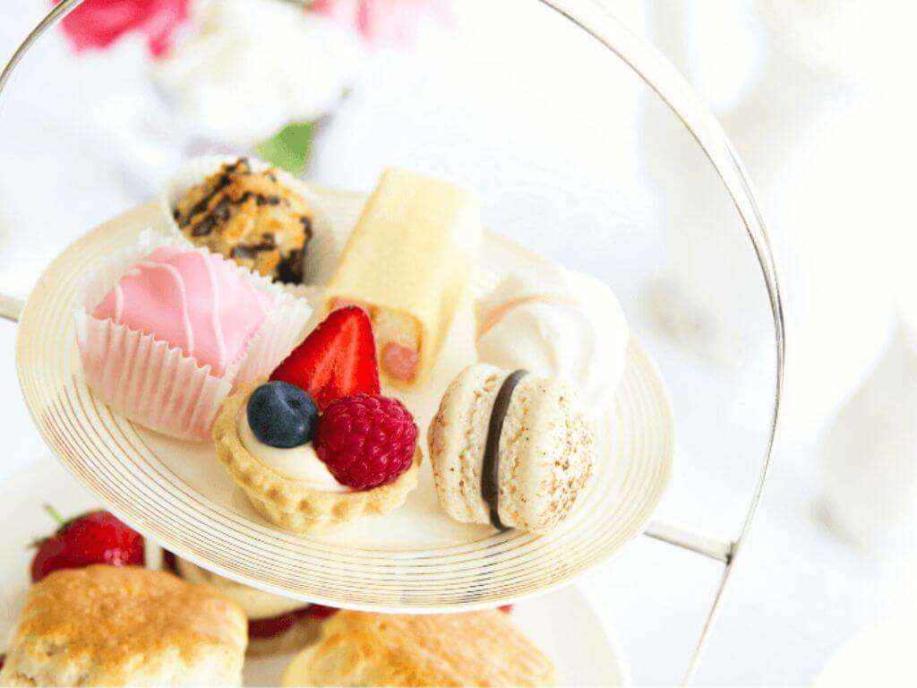 A close up picture of a cake stand with desserts on the top tier