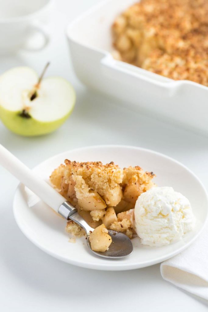 A picture of a table with a large dish of Irish Apple crumble and a smaller bowl in front with some of the crumble and ice cream