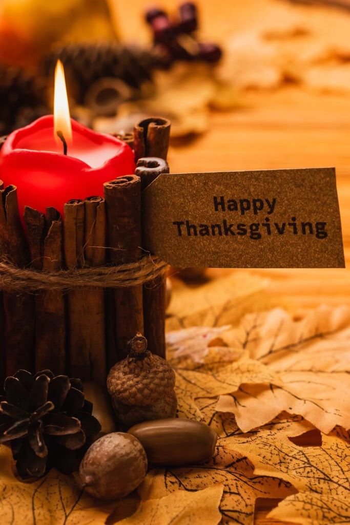 A picture of a candle surrounded by cinnamon sticks and a note saying happy Thanksgiving