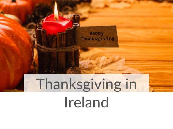 A picture of a red candle surrounded by cinnamon sticks and a note sticking out of the sticks saying happy Thanksgiving
