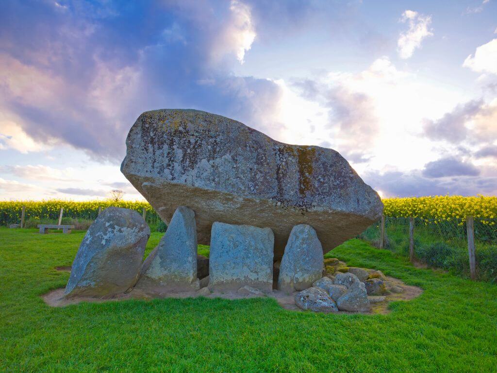 A picture of the Brownshill Dolmen Portal Tomb in Carlow with sun shining behind it, illuminating the rocks
