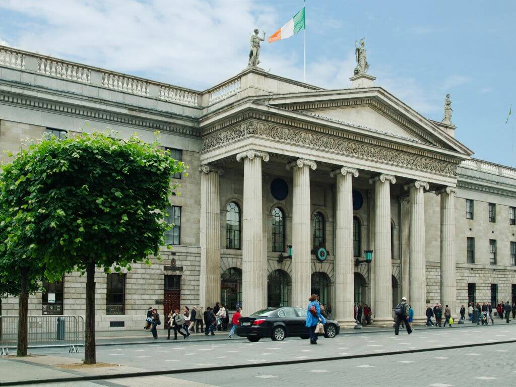 A picture of the front of the GPO in Dublin with people and cars passing in front of it