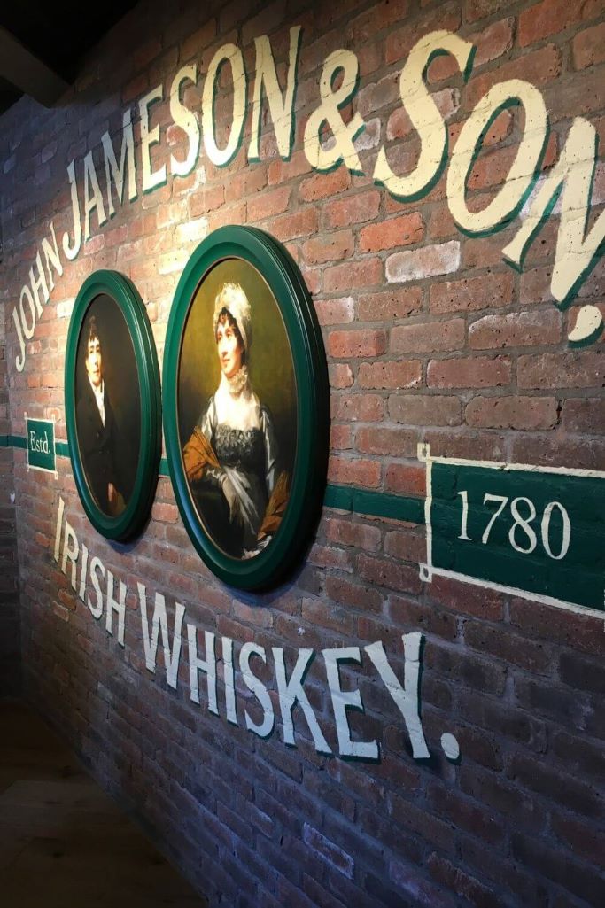 A picture of a wall with two portraits in oval picture frames, exposed brickwork and the date 1780 which you can see if you take a whiskey tour in Dublin at the Jameson Distillery
