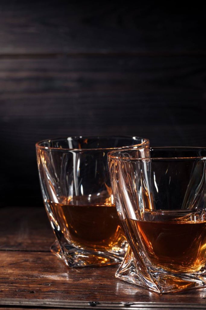 A picture of two glasses of Irish Whiskey standing side by side with a dark background