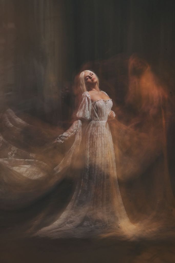 A picture of a lady with long white hair in a white dress with shadows around her depicting the image of an Irish banshee