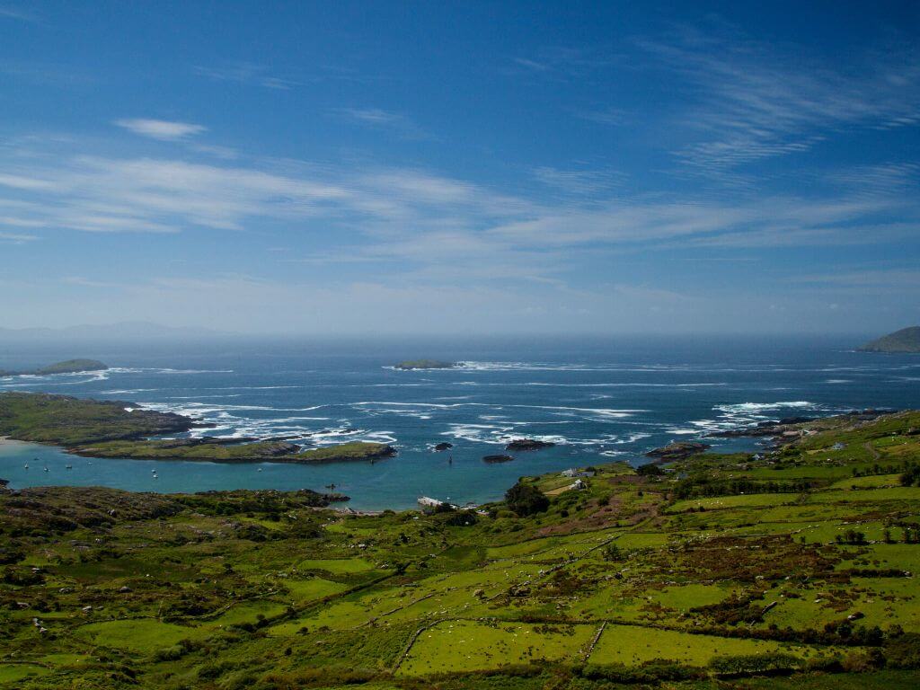 A picture of the Ring of Kerry-Wild Atlantic Way coast with blue seas in the background and green grassy fields in the foregroound