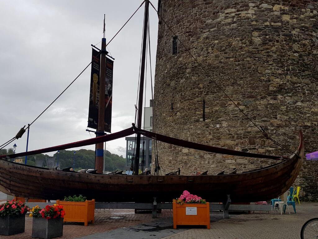 A picture of the Viking longship replica in front of Reginald's Tower in Waterford City on a grey day
