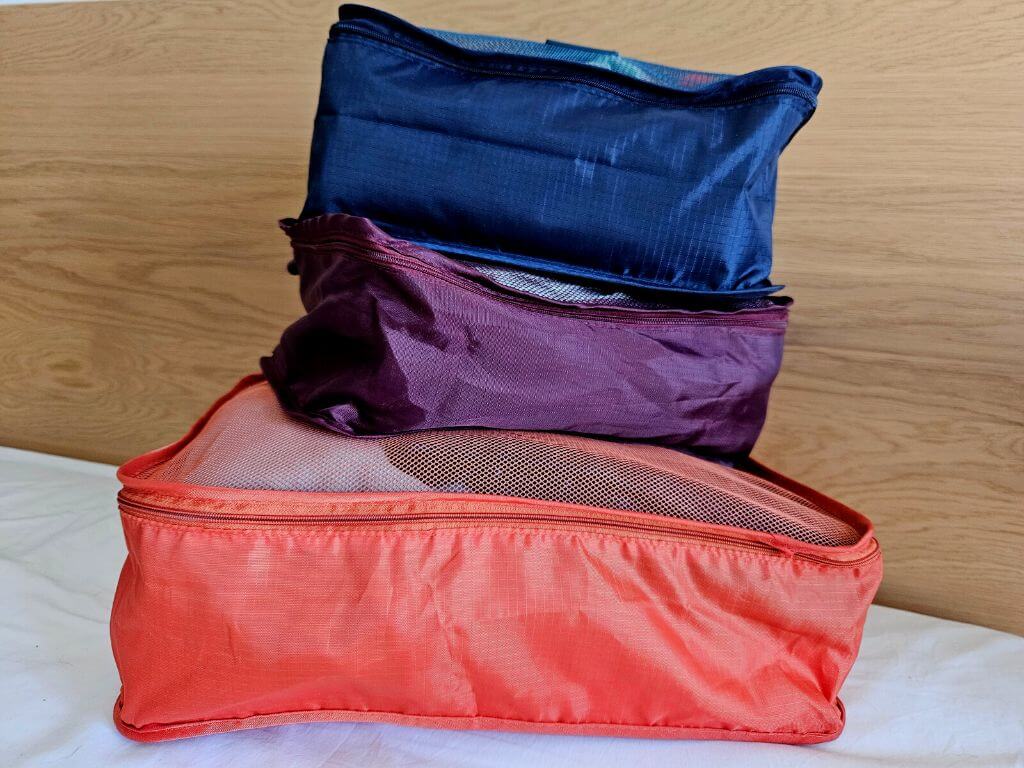 A picture of three different coloured packing cubes stacked on a bed