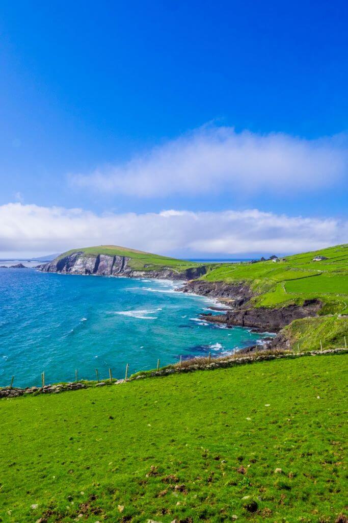 A picture of part of the west coast of Ireland on a sunny day with green fields, blue sea and blue skies overhead