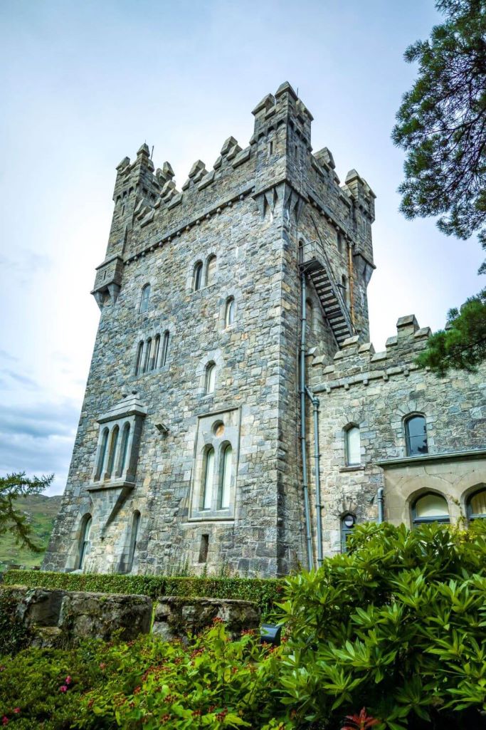 A portrait picture of Glenveagh Castle, Donegal with some green bushes in the foreground