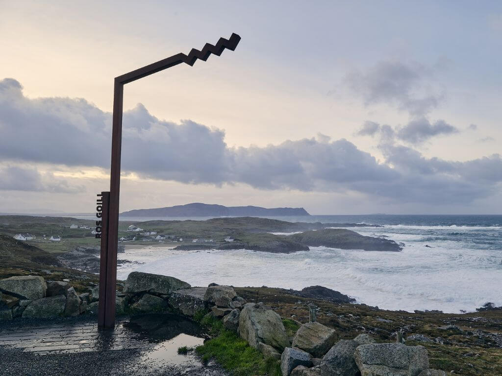 The Wild Atlantic Way sign on the Rosguill Peninsula in County Donegal with waves crashing along the shore and mountains in the background