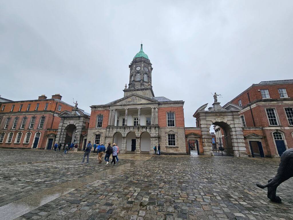 A picture taken in the courtyard of Dublin Castle featuring the Bedford Tower with people crossing in front of it on a rainy day