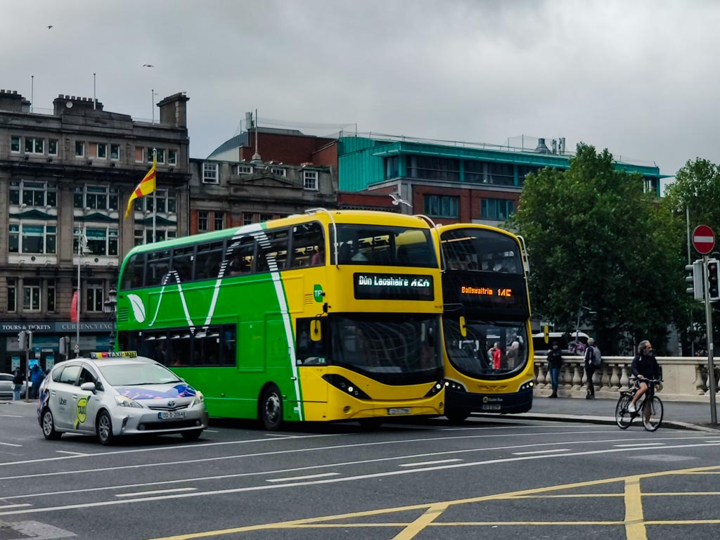 A picture of two Dublin buses and a taxi stopped at traffic lights on O'Connell Bridge heading to the south side of the city.