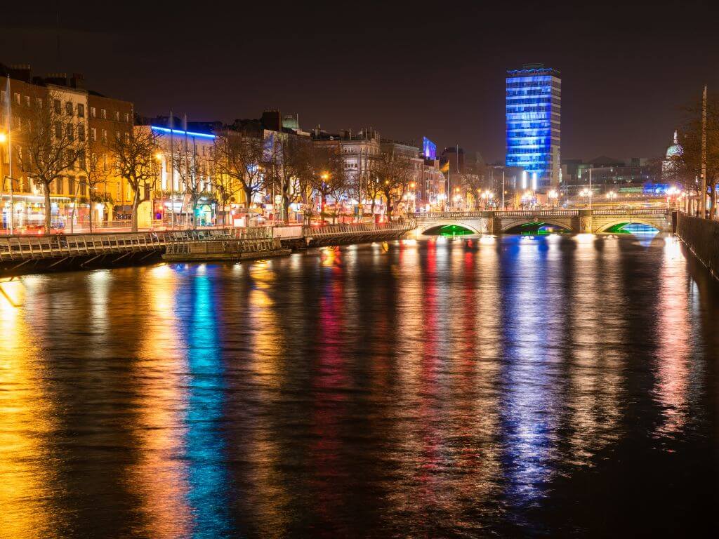 A picture looking down the river Liffey in Dublin by night with O'Connell Bridge in the background and lights reflecting off the surface of the water.