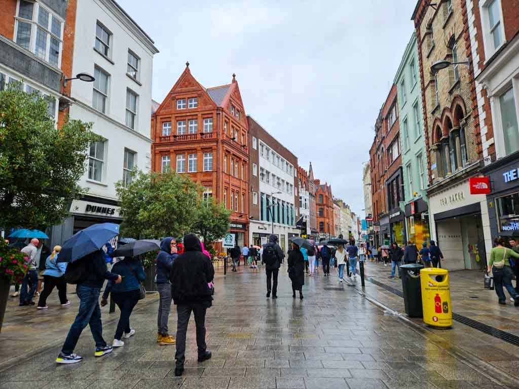 A picture of Grafton Street on a rainy day in Dublin with a few people walking along it.